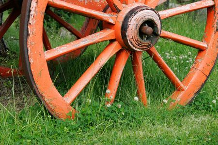 Red, wooden wagon wheel in green grassの写真素材
