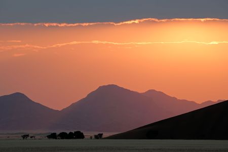 Desert sunrise with silhouettes of sand dunes, mountains and trees, Sossusvlei, Namibia, southern Africaの写真素材
