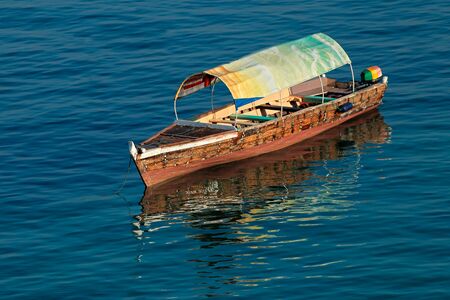 Anchored wooden boat with reflection in water, Zanzibar island