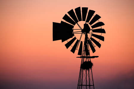 A windmill silhouetted against a red sunsetの写真素材