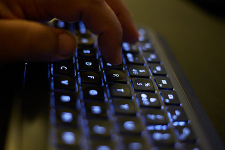 Closeup of male hands typing on laptop keyboard in dark room at night
