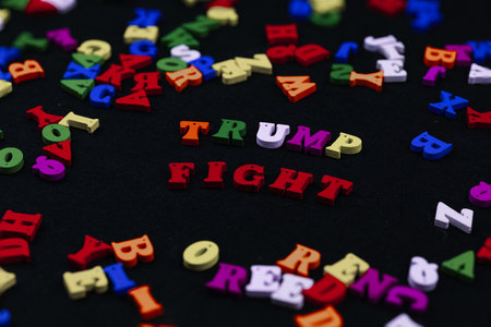 Colorful wooden letters spelling out the phrase Trump Fight against a black background, creating a...