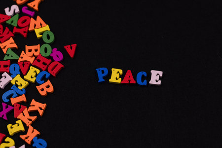 Colorful wooden letters spelling "peace" stand out against a black background, surrounded by scattered letters, creating a conceptual and striking imageの写真素材