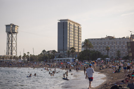 Barcelona, Spain, July 10, 2024 - Crowded beach with a distinctive tower and high-rise buildings in a coastal city during summerのeditorial素材