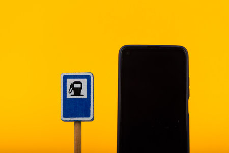 A playful wooden toy gas station sign stands next to a smartphone on a bright yellow surface. The image symbolizes the intersection of traditional and contemporary elementsの写真素材