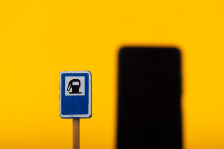 A conceptual image featuring a wooden toy gas station sign next to a blurred smartphone, set against a bright yellow background, symbolizing modern and traditional contrastsの写真素材