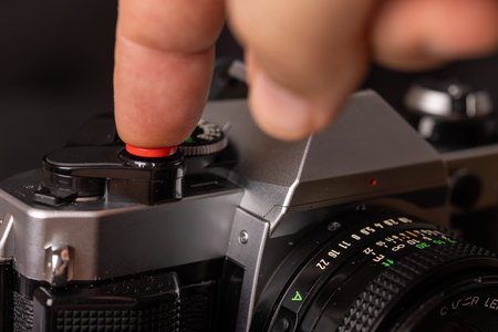 A close-up shot of an old film camera with a finger on the shutter button, contrasted against a dark...