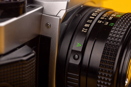 Detailed view of an old camera's lens, highlighting its intricate design and craftsmanship. Set against a bright yellow backdrop.の写真素材