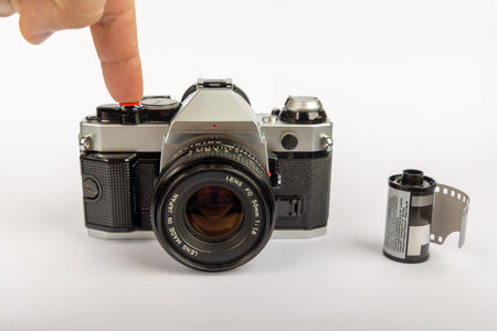 An old-fashioned camera and 35mm film rolls on a white background. The camera is centered, with a finger pressing the shutter buttonの写真素材