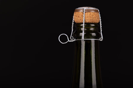 Close-up of a dark green champagne bottle neck with cork and wire cage, aligned to the right, against a black background. Ready for a festive celebration.の写真素材