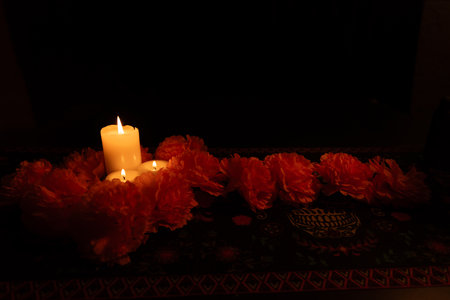 A view of three lit candles on the left, surrounded by vibrant orange marigolds, with a marigold garland framing the image. The scene is set on a DÃ­a de los Muertos tablecloth, illuminated by candlelight against a black background.の写真素材