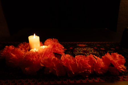 Three candles flicker on the left, decorated with a border of marigolds and a marigold garland. The black background and DÃ­a de los Muertos tablecloth create a striking visual of the celebration.の写真素材