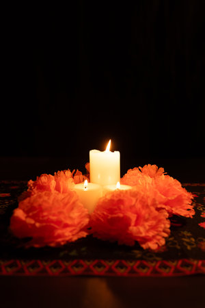 Three candles burning brightly, surrounded by marigolds on a dark background. The Day of the Dead tablecloth adds an authentic touch to this vertical photo, ideal for cultural celebrations.の写真素材