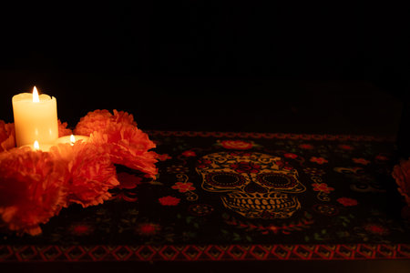 Three lit candles on the left, surrounded by vibrant orange marigolds, with a black backdrop. The scene is softly illuminated by the candlelight, set atop a DÃ­a de los Muertos tablecloth for a festive touch.の写真素材