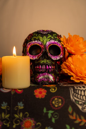 A detailed skull adorned with metallic flowers, surrounded by vibrant orange marigolds. An illuminated candle is beside it, set against a vertical gradient white background. Perfect for Day of the Dead themesの写真素材