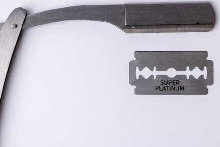 Top-down view of an open straight razor with a sharp barber's blade, set against a clean white background. The focus is on the fine craftsmanship of the razor and its edgeの写真素材