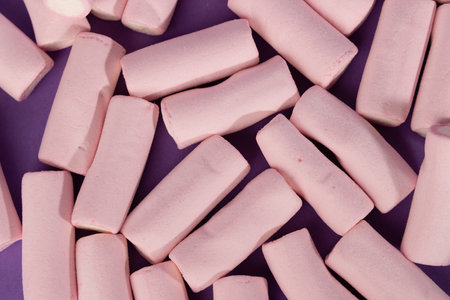 A detailed top view of disorganized marshmallows, occupying the left side of the horizontal photo. The marshmallows create a playful, colorful scene set against a deep purple backgroundの写真素材