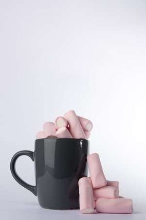 A vertical shot of a gray mug full of marshmallows, paired with a small mound of marshmallows in the center, all against a white backgroundの写真素材