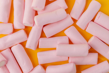 From a top view, this horizontal image features a messy arrangement of marshmallows taking up the top part of the frame. The bright yellow background enhances the visual contrast and appeal.の写真素材