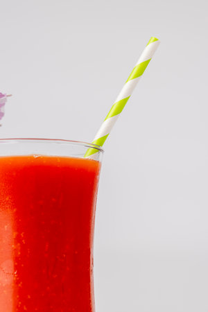 Detailed shot of a cocktail with a green straw, positioned in the center of the horizontal frame. The stark white background emphasizes the vibrant colors of the drinkの写真素材