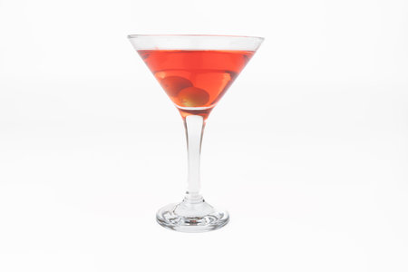 A horizontal image showing a cocktail glass with a red drink and two olives. The glass is positioned on the left of a white background, highlighting the rich color and garnishes of the drinkの写真素材