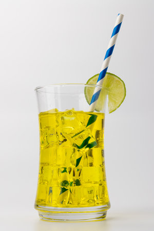 vertical photo of a vibrant yellow lemonade drink with ice cubes and a lemon slice garnish. A blue straw completes the refreshing look, all set against a white backgroundの写真素材