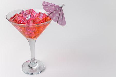 A top-down shot of a refreshing pink lemonade cocktail filled with ice and topped with a colorful paper umbrella. The image is horizontally aligned against a white backgroundの写真素材