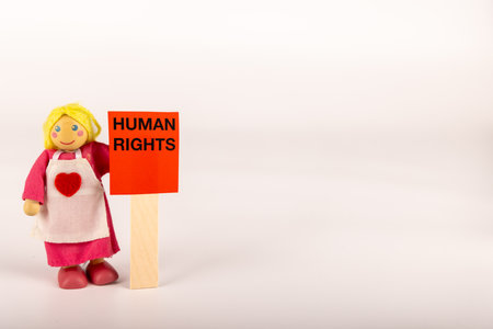 A wooden doll clutches a red card that reads "Human Rights." The image is presented horizontally against a white backdrop, underlining the significance of human rightsの写真素材
