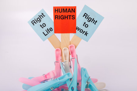 Clothespins are arranged neatly on a red sign that reads "Human Rights" in bright red. The sign is set against a plain white backdrop, making the message clearの写真素材