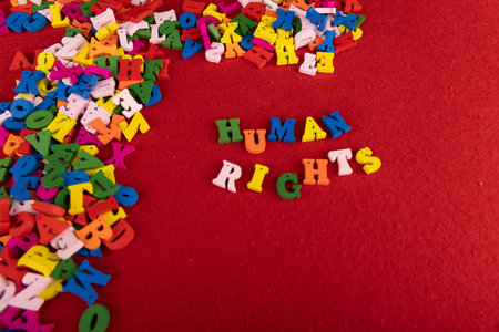 A bright composition of wooden letters forms "Human Rights," with a random pile of colorful letters on the left, all set on a striking red backdropの写真素材