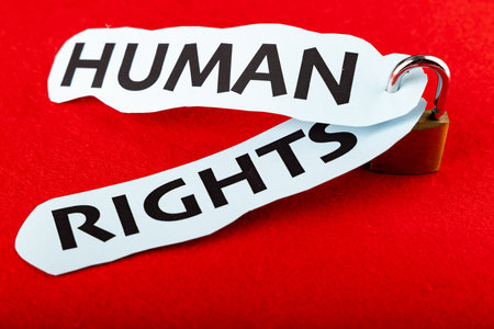 A detailed padlock holds two pieces of paper labeled "human rights," placed in the center of the image with a strong red backgroundの写真素材