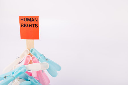 Clothespins are arranged neatly on a red sign that reads "Human Rights" in bright red. The sign is set against a plain white backdrop, making the message clearの写真素材