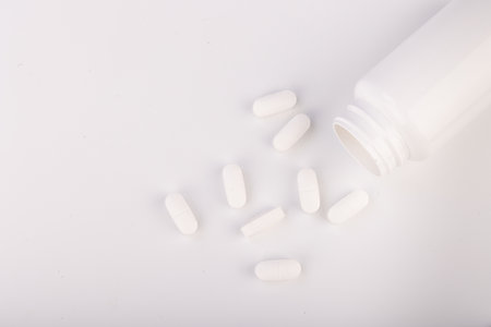Detailed overhead view of a white bottle with white tablets positioned on the left. A pristine white background emphasizes the medical and hygienic aspectsの写真素材