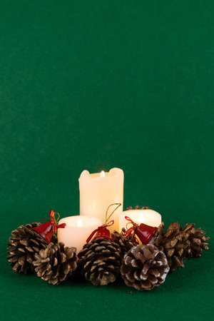 A charming Christmas centerpiece with bright candles, decorative pinecones, and red bells, set against a rich green backdropの写真素材