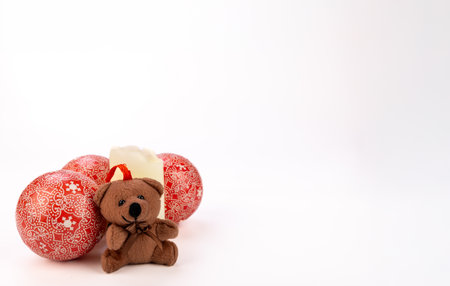 A Christmas-themed arrangement with a lit candle, a cute teddy bear, and festive ornaments on a white background, creating a cozy holiday atmosphereの写真素材
