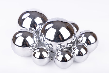A set of shiny silver Christmas balls in multiple sizes placed on a white background, creating a simple yet festive scene for the holiday seasonの写真素材