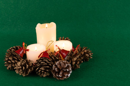 A delightful holiday table arrangement featuring candles, pinecones, and red bells, enhancing the festive spirit on a green surfaceの写真素材