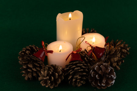 A whimsical holiday centerpiece showcasing lit candles, pinecones, and red bells, enhancing the festive spirit on a green backgroundの写真素材