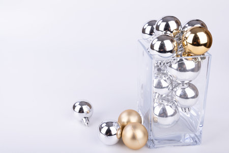 A glass jar filled with various sizes of silver and gold ornaments, surrounded by festive decorations on a white backgroundの写真素材