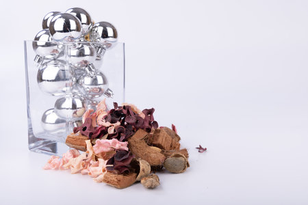 A beautiful glass jar filled with silver balls of various sizes, complemented by dried flowers, perfect for holiday decor on a white backgroundの写真素材