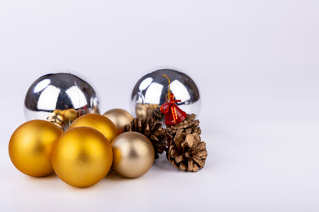 Pinecones beautifully decorated with bright red bells and golden-silver Christmas ornaments of varying sizes, set against a clean white backgroundの写真素材
