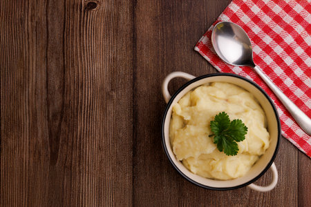 Mashed potatoes served in a bowl with fresh potatoes and a red napkin, all on a brown wooden tableの写真素材