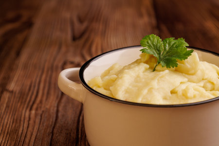 Freshly prepared mashed potatoes in a bowl on a wooden table. The creamy texture and warm appearance...