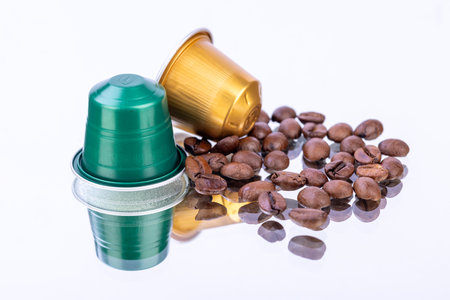 Various coffee capsules and beans arranged on a mirror, reflecting vibrant colors and textures over...