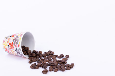 A perfectly brewed cup of coffee placed next to a generous pile of coffee beans on a pristine white backgroundの写真素材