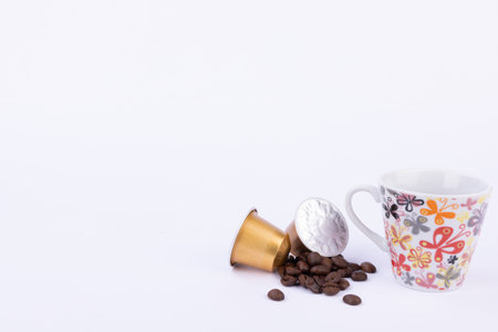 Two golden coffee capsules sit beside coffee beans and a steaming cup of coffee, showing a perfect morning brewの写真素材