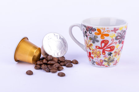 A bright setup showcasing golden coffee capsules, scattered coffee beans, and a cup, perfect for coffee enthusiastsの写真素材