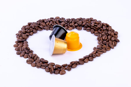 A heart shape crafted from coffee beans, showcasing coffee capsules at the center, set against a clean white backgroundの写真素材