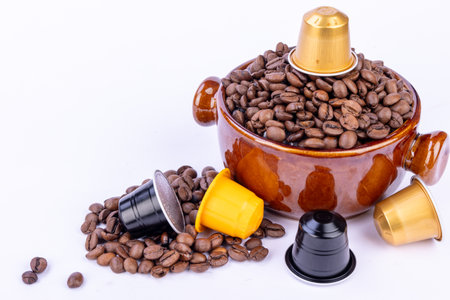 Brown bowl filled with coffee beans and a capsule on top, surrounded by scattered beans and colorful capsules on a white backgroundの写真素材
