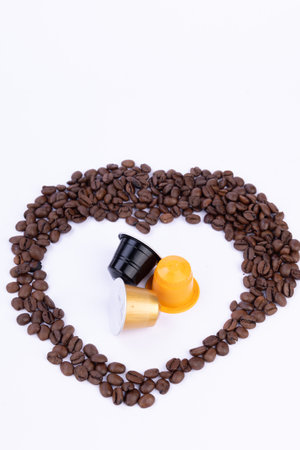 An artistic heart made from coffee beans, featuring coffee capsules in the middle, beautifully displayed on a white surfaceの写真素材